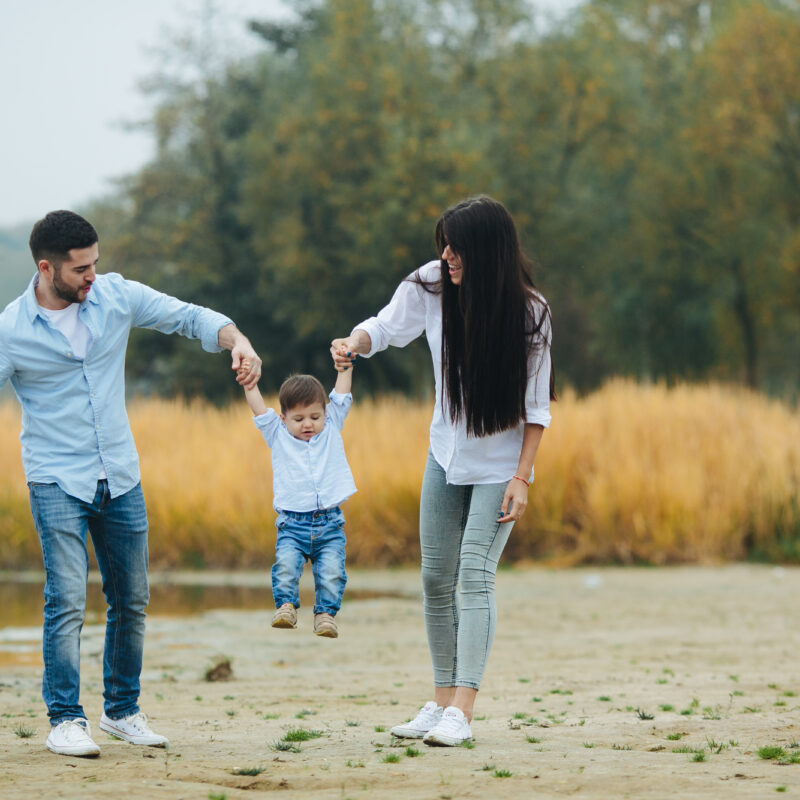 A heartwarming, sun-drenched photograph of a joyful family—a father, mother, and young child—outdoors at dusk. The parents hold the child's hands, lifting him as they smile. Integrated into the image is large, elegant text that reads: 'A Legacy That Outlives You' followed by, 'Create a meaningful impact that echoes through time. We help you preserve your wealth so it continues to nurture, educate, and empower your children and grandchildren.' This visual and message represent the core values and generational protection provided by an Octowill Family Trust.