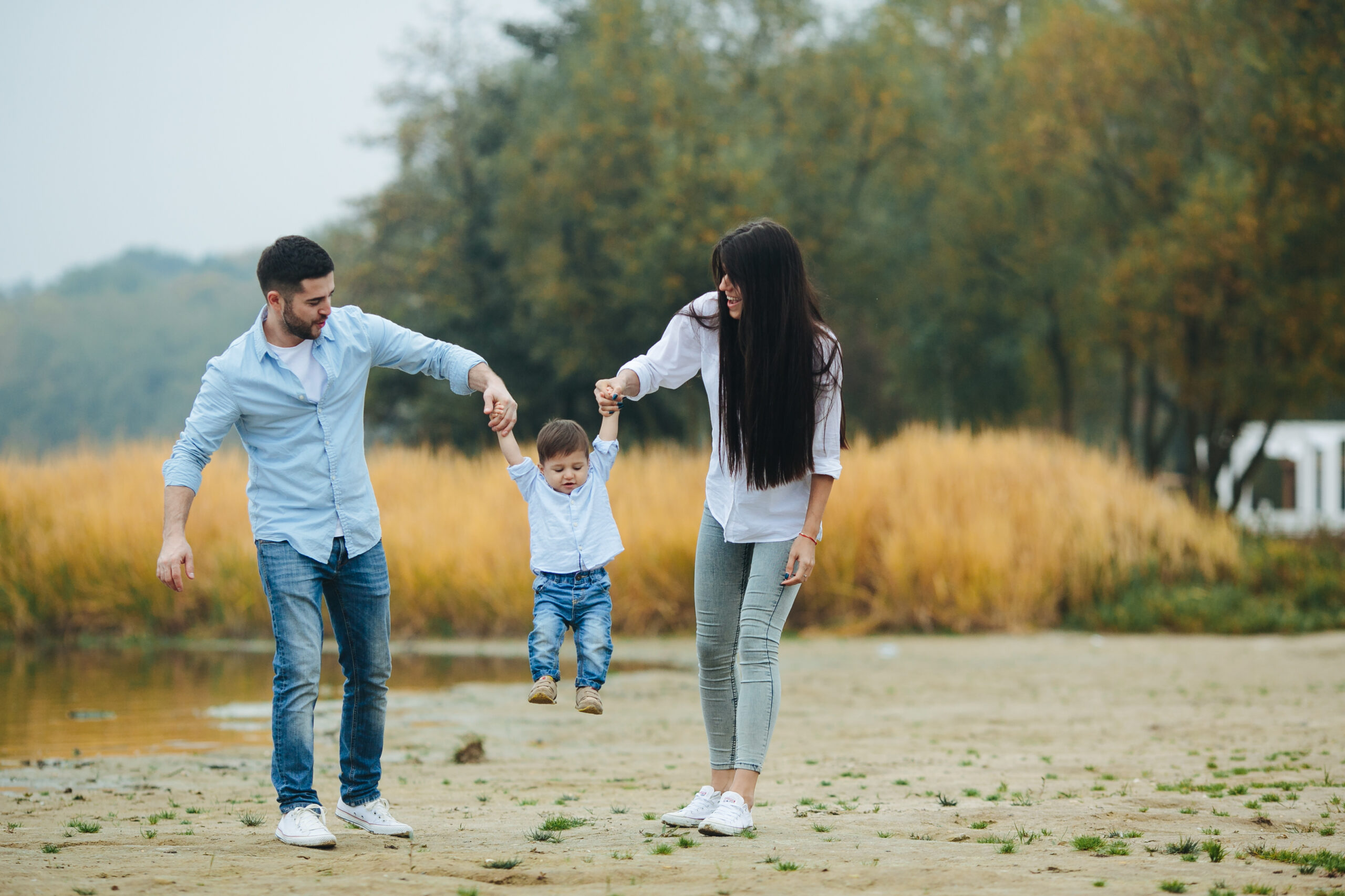 A heartwarming, sun-drenched photograph of a joyful family—a father, mother, and young child—outdoors at dusk. The parents hold the child's hands, lifting him as they smile. Integrated into the image is large, elegant text that reads: 'A Legacy That Outlives You' followed by, 'Create a meaningful impact that echoes through time. We help you preserve your wealth so it continues to nurture, educate, and empower your children and grandchildren.' This visual and message represent the core values and generational protection provided by an Octowill Family Trust.